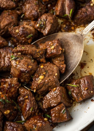 A serving spoon scooping into a plate filled with steak bites