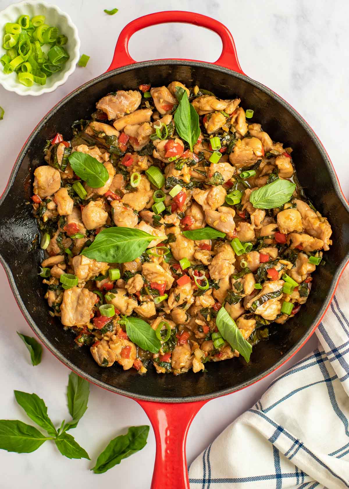 overhead shot of thai basil chicken in a skillet, garnished with fresh basil and chopped scallions