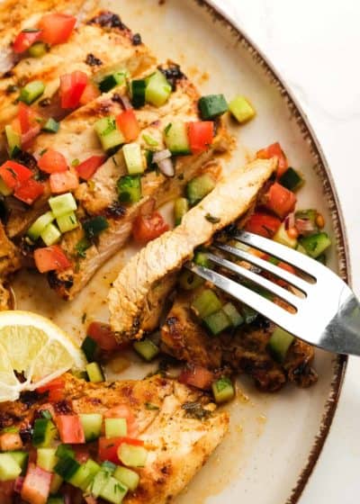 juicy greek chicken with cucumber salsa on a plate with lemon wedges